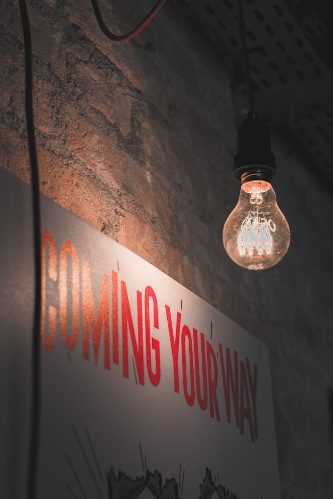 A dimly lit vintage bulb hanging against a rustic brick wall with 'COMING YOUR WAY' sign, evoking urban vibes.