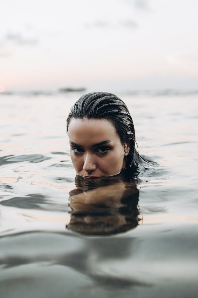 Woman partially submerged in tranquil waters at twilight, exuding calm and tranquility.